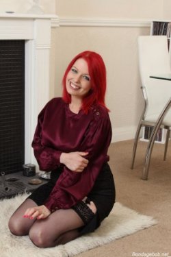 Temptress Kate smiling in a silk blouse skirt and stocking waiting for bondage
